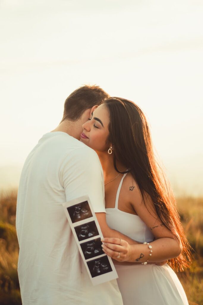 A loving couple embraces outdoors, holding ultrasound images, symbolizing their future family.