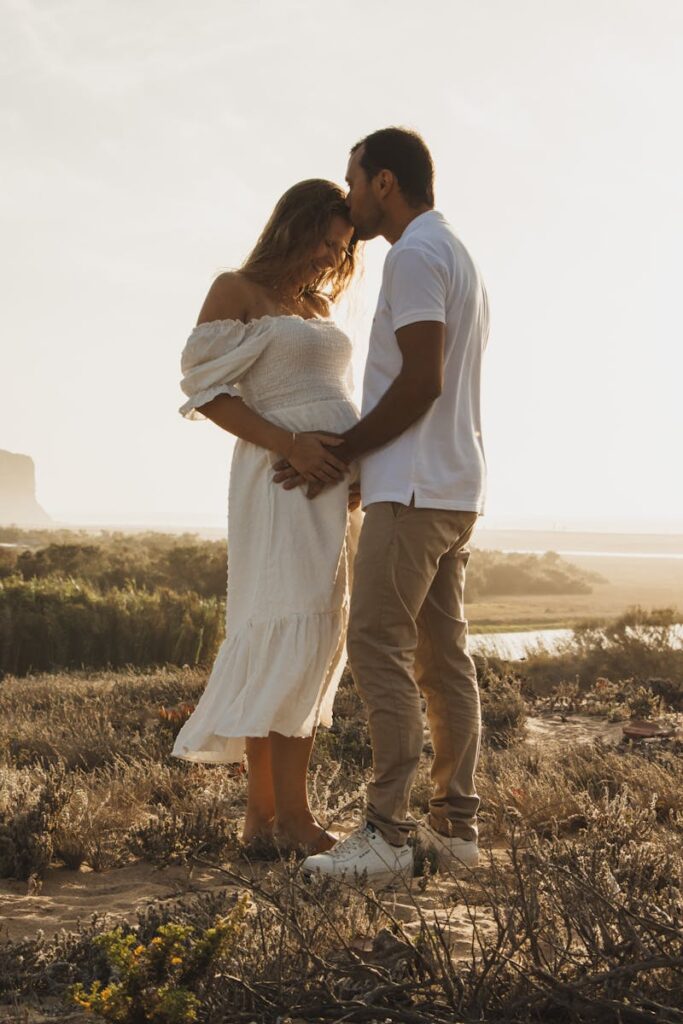 Expectant couple embracing on a serene beach during sunset, radiating love and happiness.