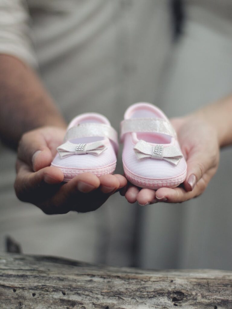 Close-up of parents holding delicate pink baby shoes, symbolizing an upcoming arrival.